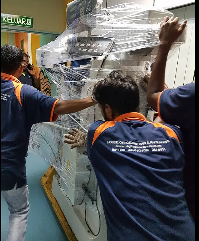 Crew guiding a shrink-wrapped milling machine through a corridor