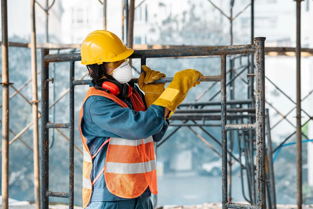 Worker wearing a hard hat and protective gloves fitting a scaffold frame